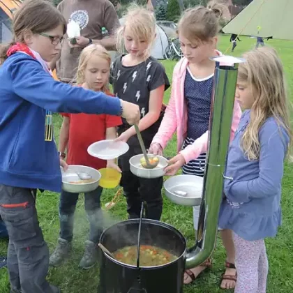 Kinder füllen draußen ihre Teller an einem großen Topf