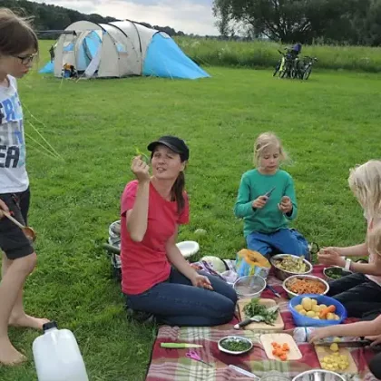Betreuerin und Kinder beim Essen auf dem Rasen