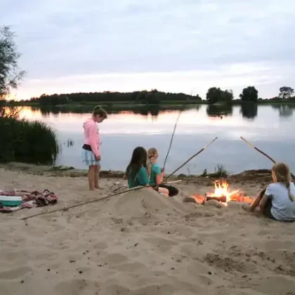 Kinder sitzen mit Stockbrot beim Lagerfeuer am Strand