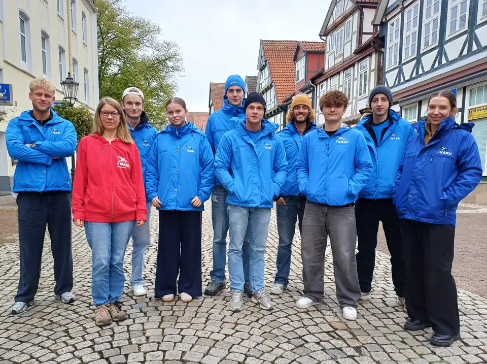 Das Werberteam für den NABU Hermannsburg/Faßberg e.V. (hellblaue Jacken) Eine Gruppe von 10 jungen Personen steht auf einer Kopfsteinpflaster-Straße mit Fachwerk-Häusern an beiden Seiten